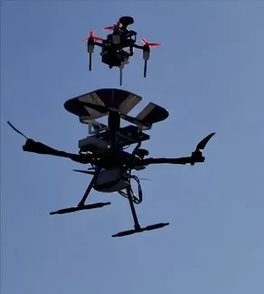 A smaller receiver drone hovering above the larger supplier drone during an outdoor docking demonstration.